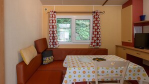 Habitación pequeña con sofá, una mesita con mantel estampado, televisión y ventana con cortinas.