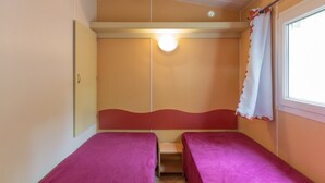 Una habitación con dos camas, una ventana con cortina, una lámpara y una puerta.
