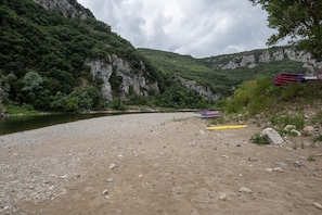 A riverbank with a rocky shore, a cliff with greenery, and several kayaks.