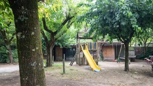 Un parque infantil con un tobogán amarillo, rodeado de árboles y estructuras de madera.