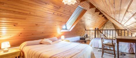 A cozy attic bedroom with a sloped ceiling, a bed, a desk, and a chair.