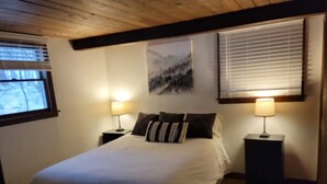 Ein Schlafzimmer mit einem Bett, zwei Nachttischen inklusive Lampen, einem Fenster mit Jalousien und einem Bild an der Wand.