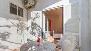 A small outdoor patio with a wicker table and chair, a bottle of wine, and a sliding door leading to an interior space.