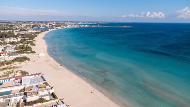An aerial view of a coastal area with a beach, buildings, and a clear sky.