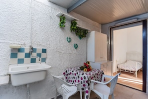 A bathroom with a sink, a white chair, a table with a polka dot tablecloth, and a bed in the adjacent room.