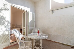 A small outdoor seating area with wicker chairs and a table, a bottle of wine, and a door leading to a room.