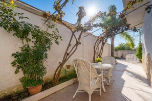 Un patio con una mesa y sillas, rodeado de plantas y una pared blanca.