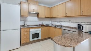 Een moderne keuken met houten kastjes, een witte koelkast, een fornuis, een magnetron en een spoelbak.