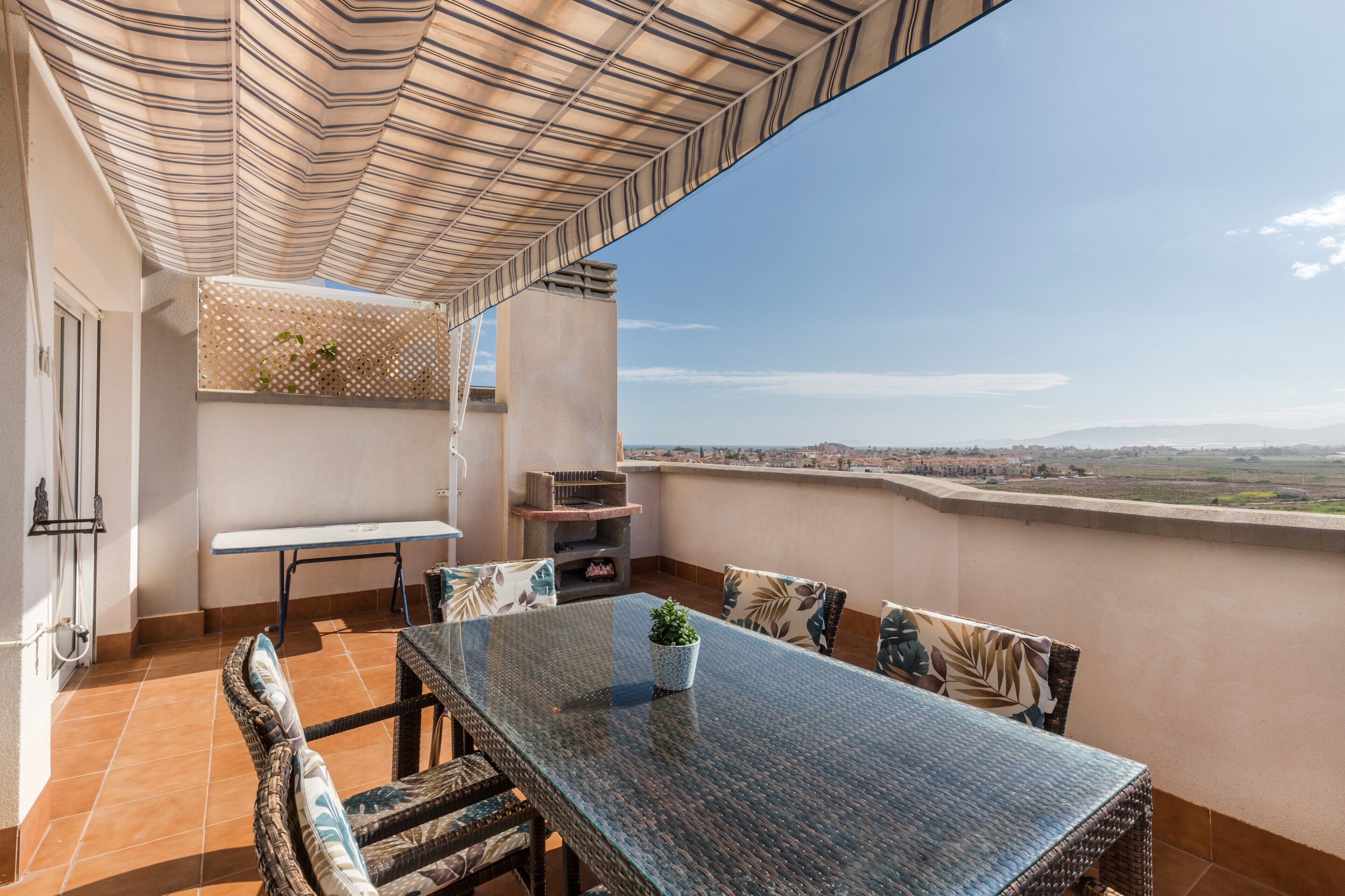 Un balcón con mesa y sillas, un toldo a rayas y vistas al paisaje.