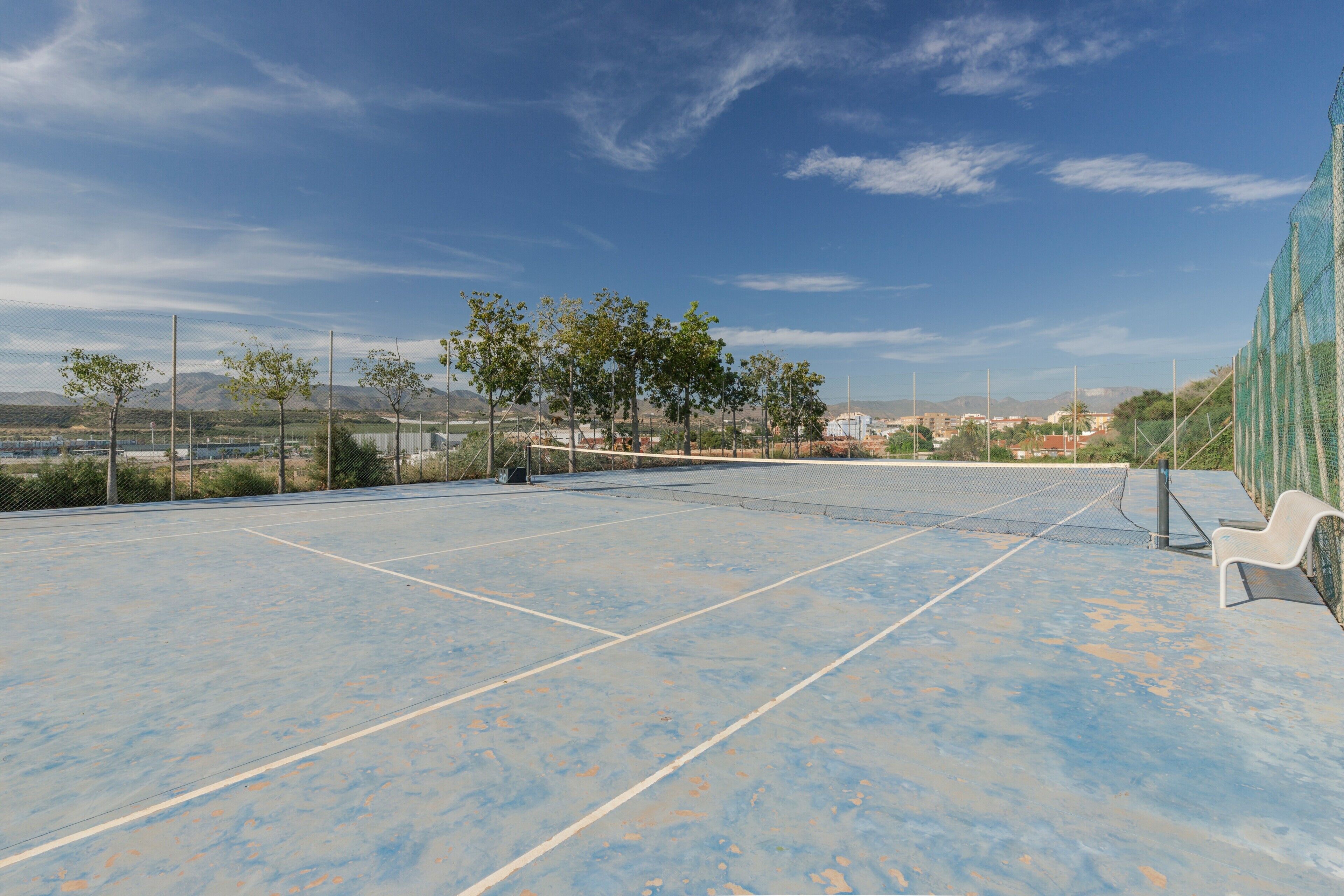 Een tennisbaan buiten met net, zitgedeelte en omrastering.