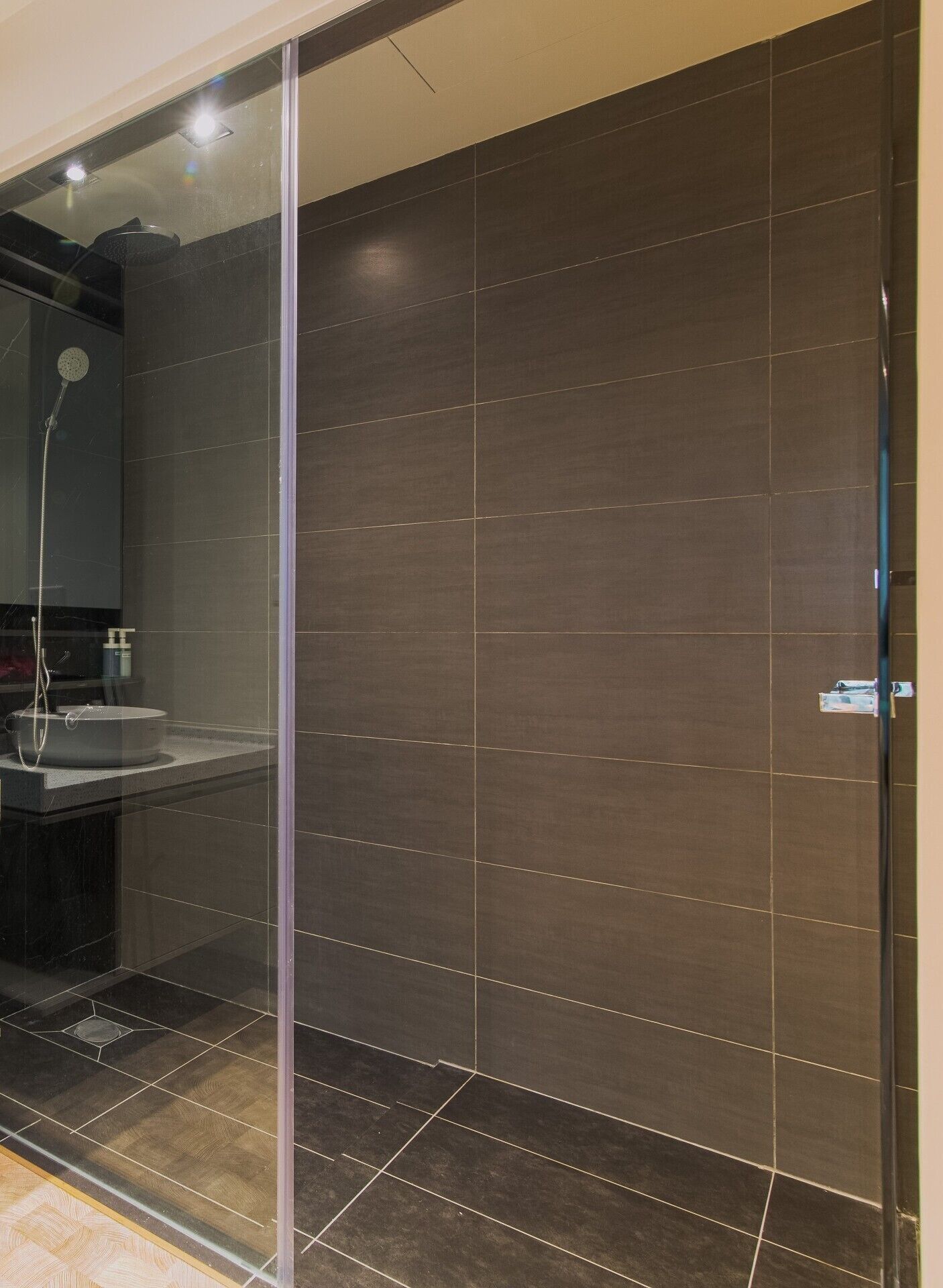 A modern bathroom with a glass shower enclosure, dark tiles, and a visible sink area.