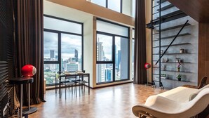 Ein geräumiges Wohnzimmer mit großen Fenstern und Blick auf die Stadt, einer modernen Treppe und einer minimalistischen Möblierung.