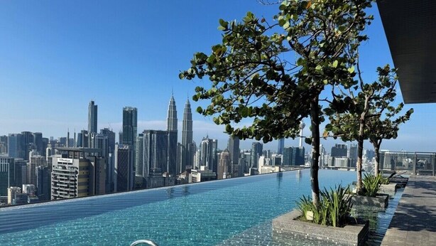Ein Pool im Unendlickkeitsstil mit Blick auf eine Stadtlandschaft, einem Baum und einem klaren Himmel.