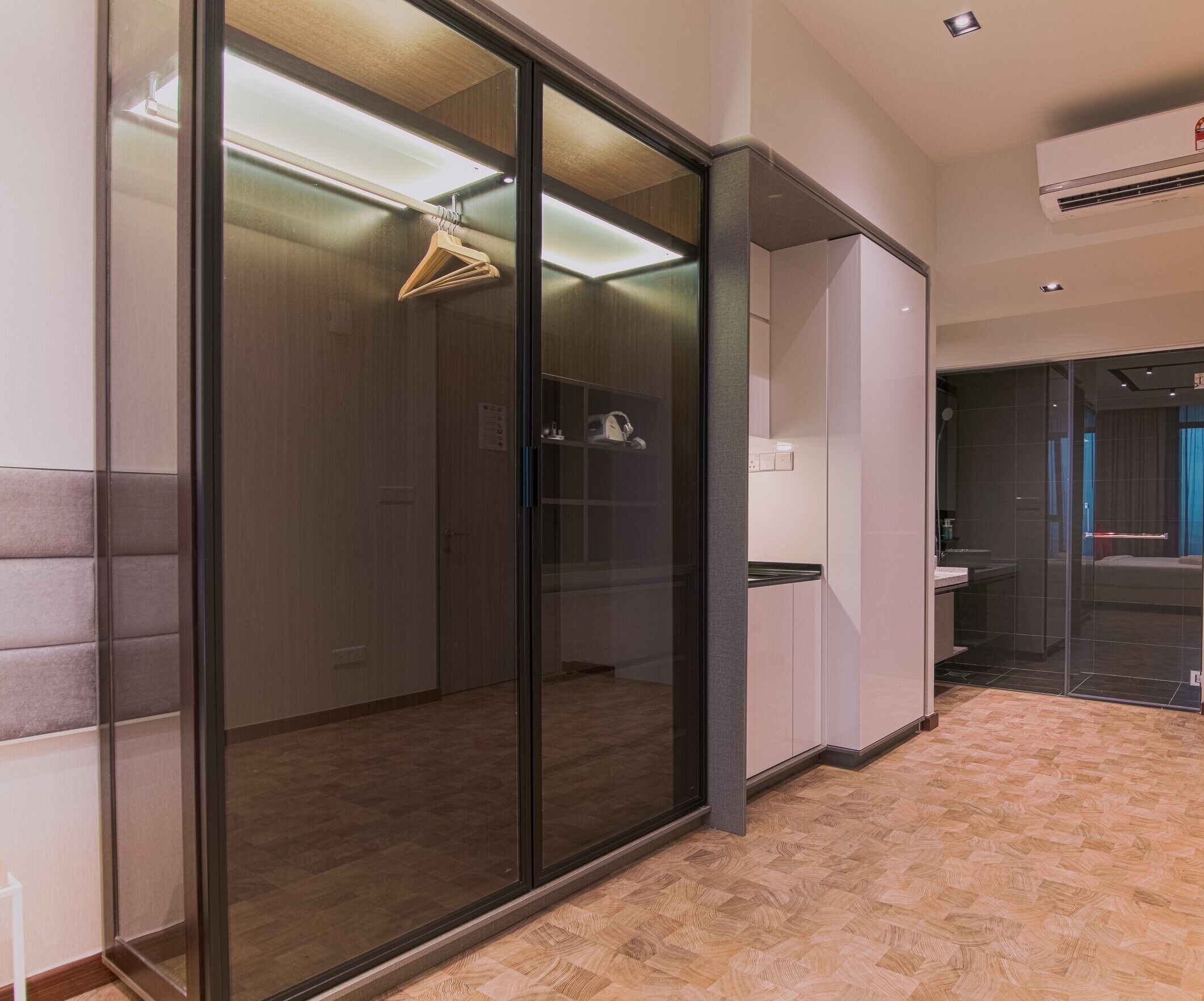 Une chambre d’hôtel moderne dotée d’une porte-fenêtre coulissante, d’un plancher en bois, d’une petite kitchenette et d’un espace douche.