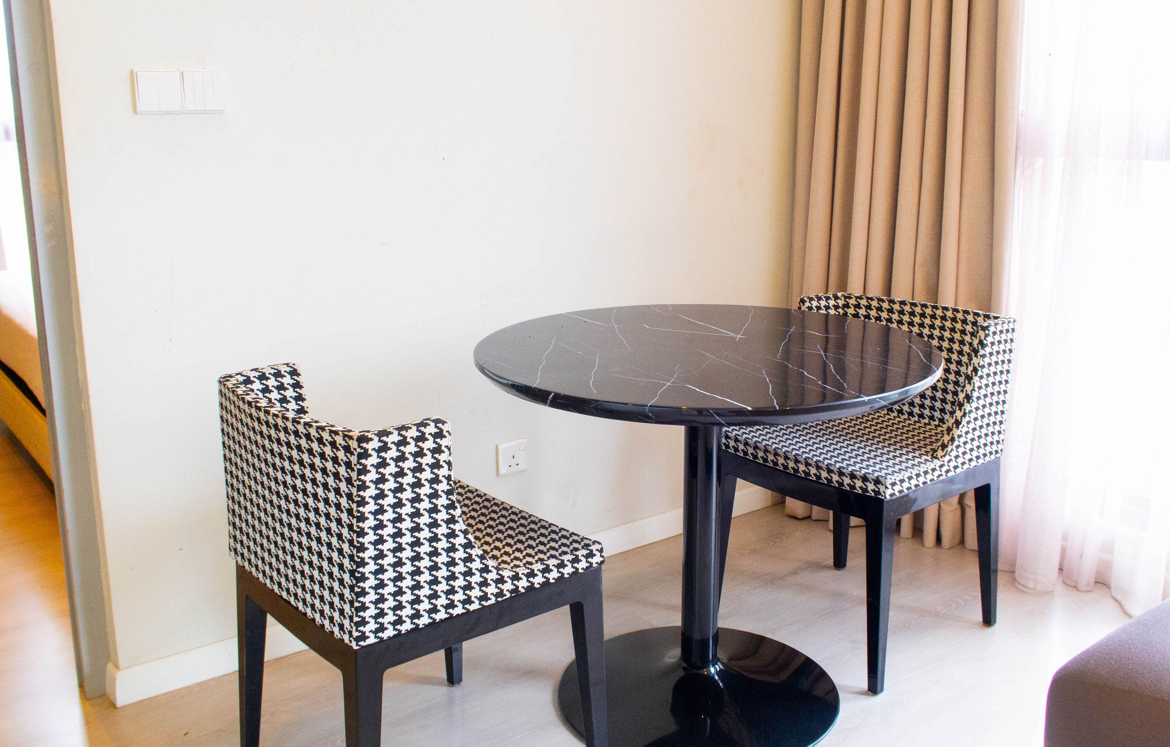 A room with a round table and two patterned chairs, a light switch, and a curtain.