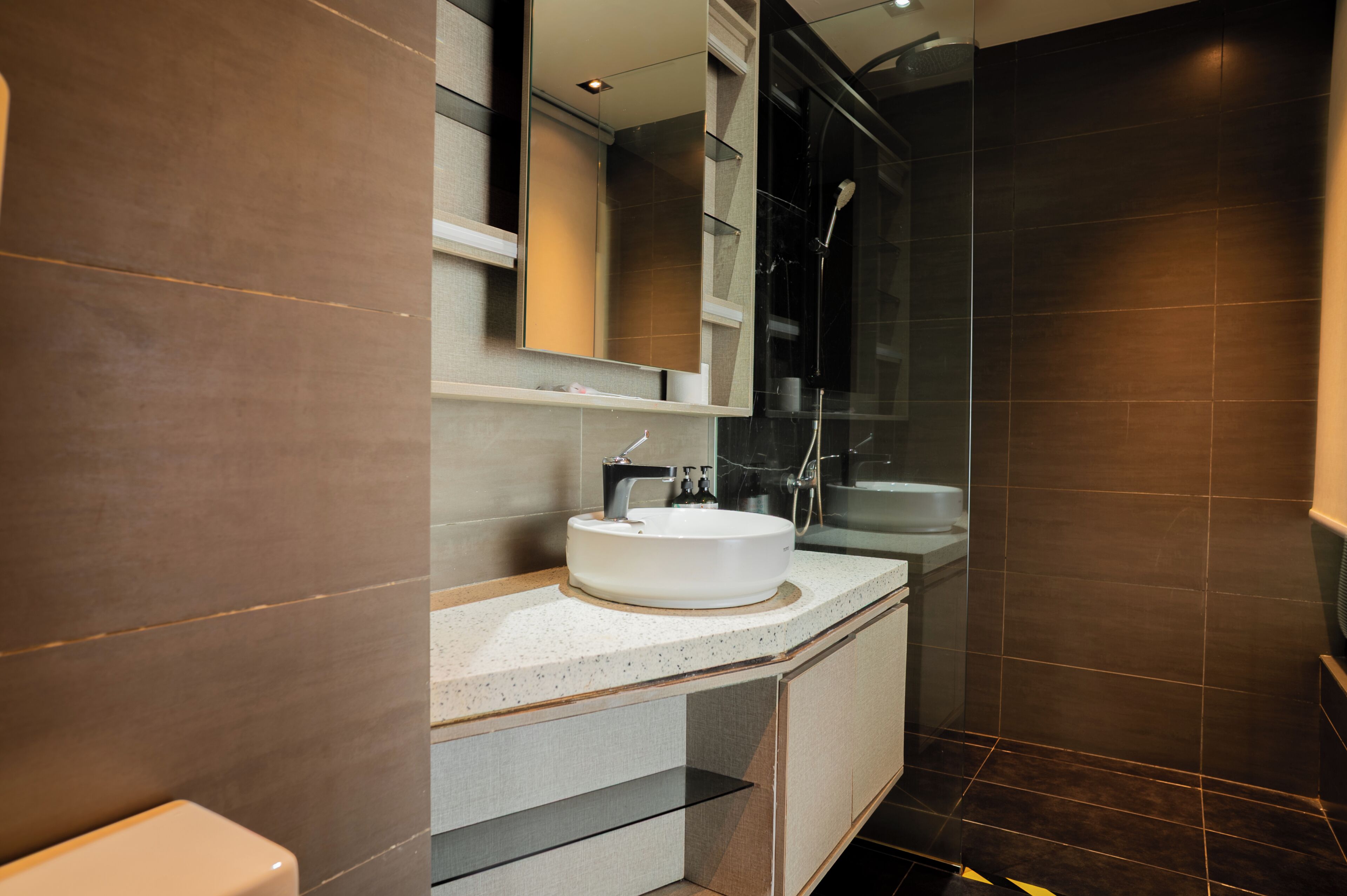 A modern bathroom with a white sink, a glass shower enclosure, and dark tiled walls.
