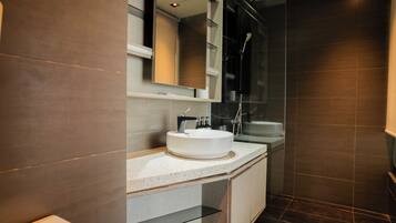 A modern bathroom with a white sink, a glass shower enclosure, and dark tiled walls.
