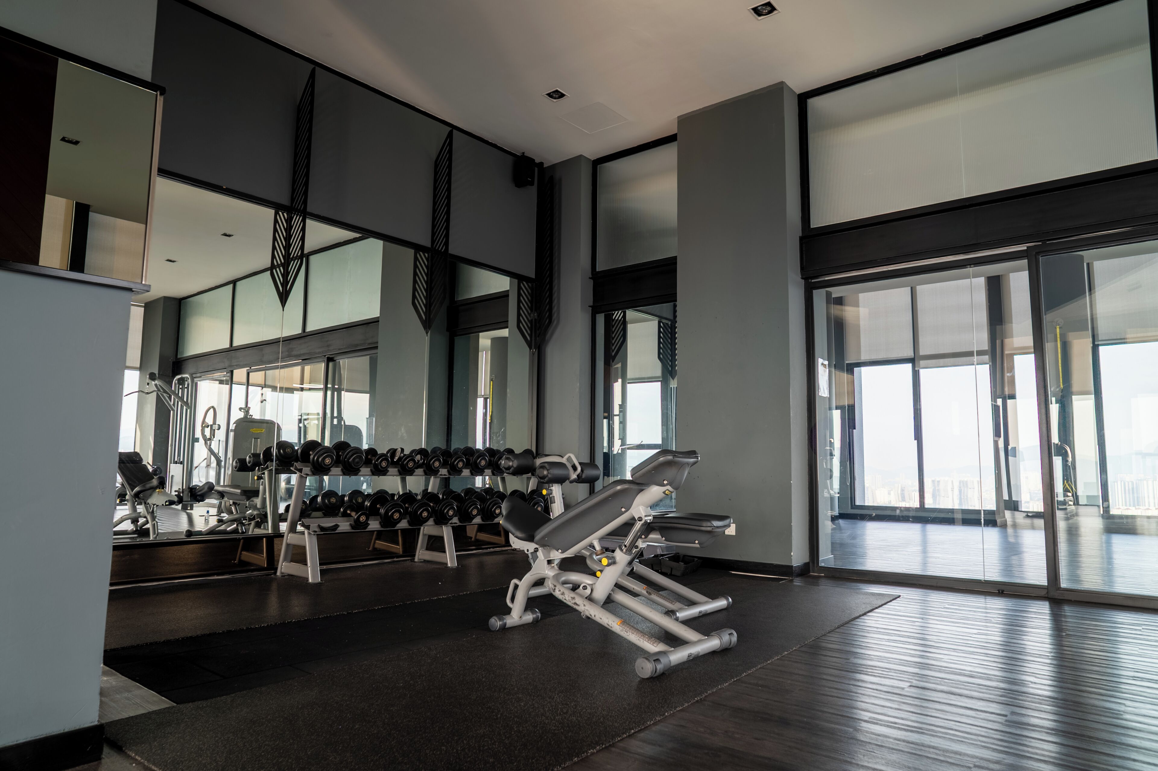 Une salle de sport moderne équipée de matériel d’exercice, dotée de grandes fenêtres et d’un mur recouvert de miroirs.