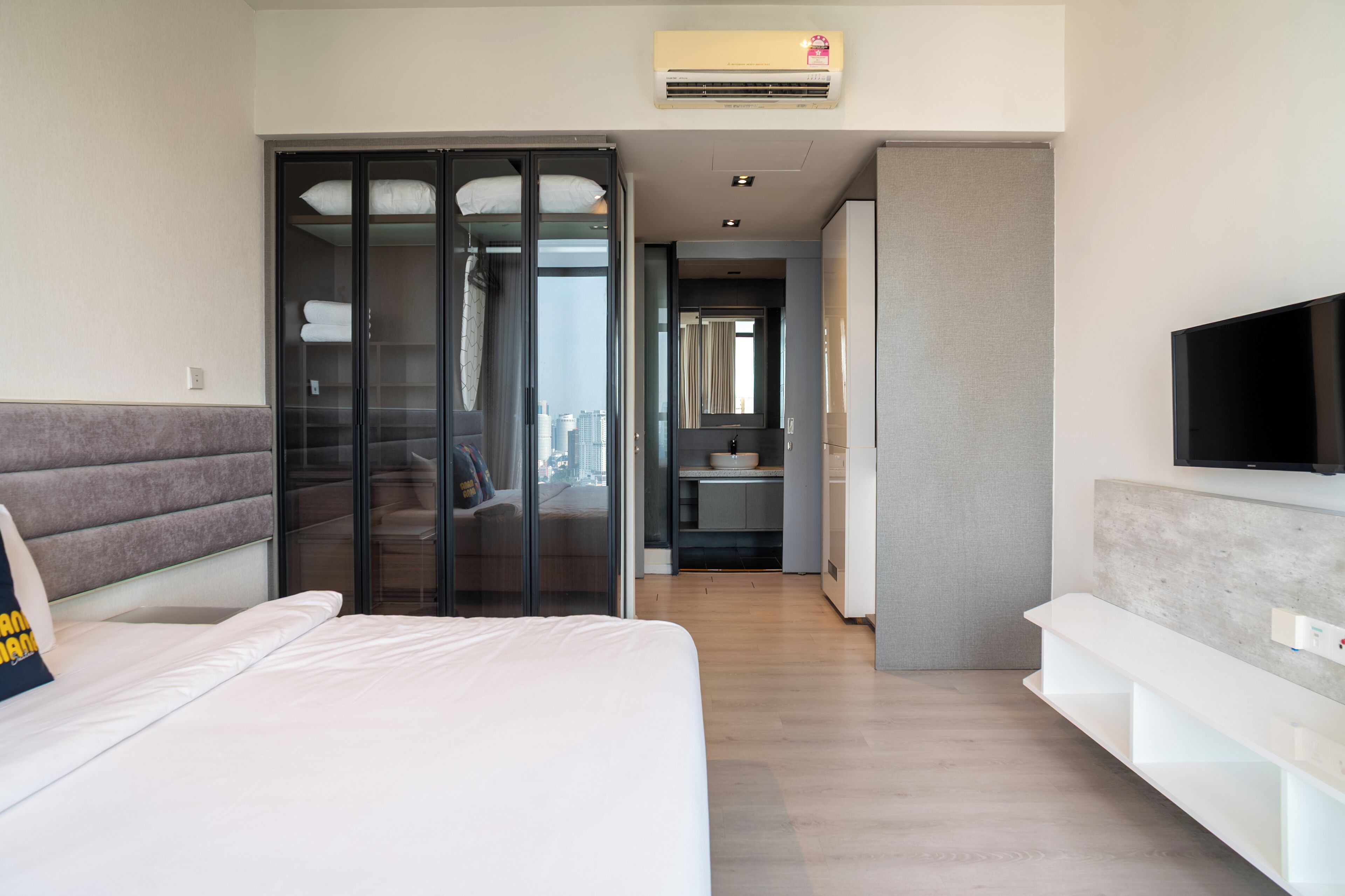 Camera d'albergo moderna con un letto, una TV a parete, un armadio e un bagno visibile attraverso una porta aperta.