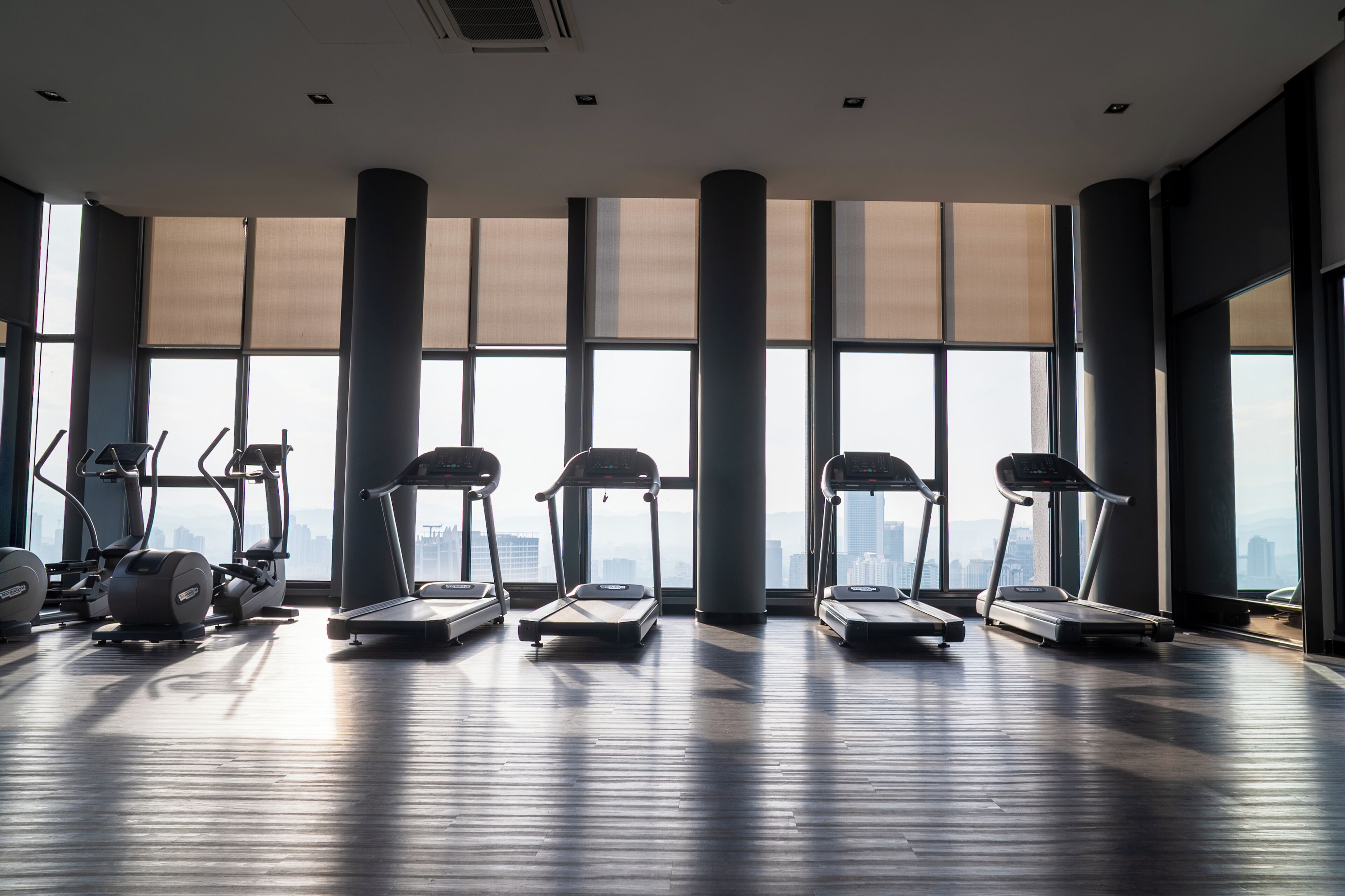 Un gimnasio con cintas de correr y elípticas, ventanas amplias y vistas a la ciudad.