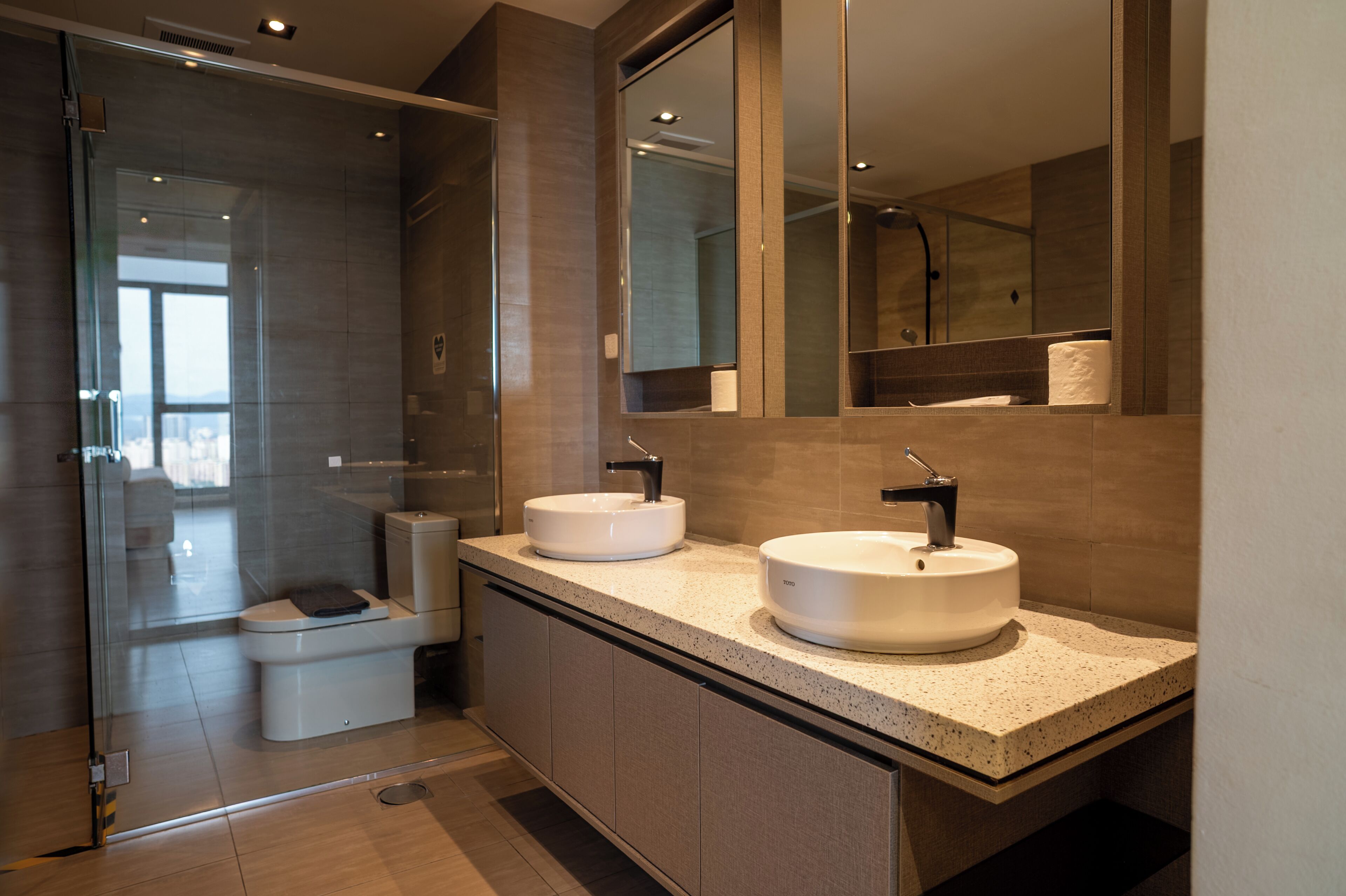 A modern bathroom with two sinks, a glass shower enclosure, and a toilet.