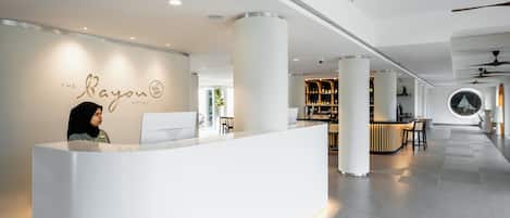 Un espace d’accueil moderne, au design épuré et minimaliste, comprenant un comptoir d’accueil, un coin salon et un bar/lounge avec des étagères remplies de bouteilles.