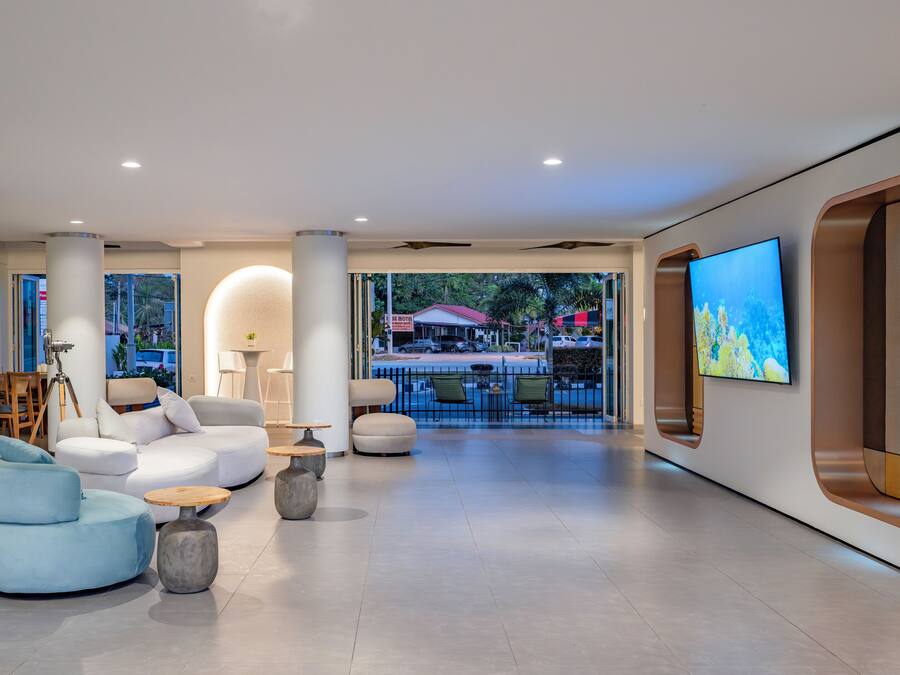 A modern hotel lobby with a seating area, a large TV screen, and a view of the outside.
