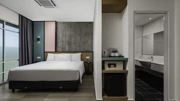 A modern hotel room with a large bed, a desk with a coffee maker, a small kitchenette, and a bathroom with a mirror and sink.