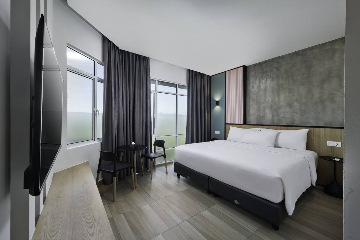 Une chambre d’hôtel moderne dotée d’un grand lit, d’un bureau avec une chaise, d’une petite table et d’une grande fenêtre avec des rideaux.