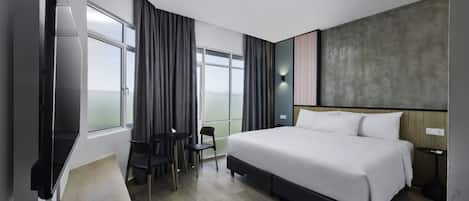 Una habitación de hotel moderna con una cama grande, un escritorio con silla, una mesita pequeña y un ventanal con cortinas.