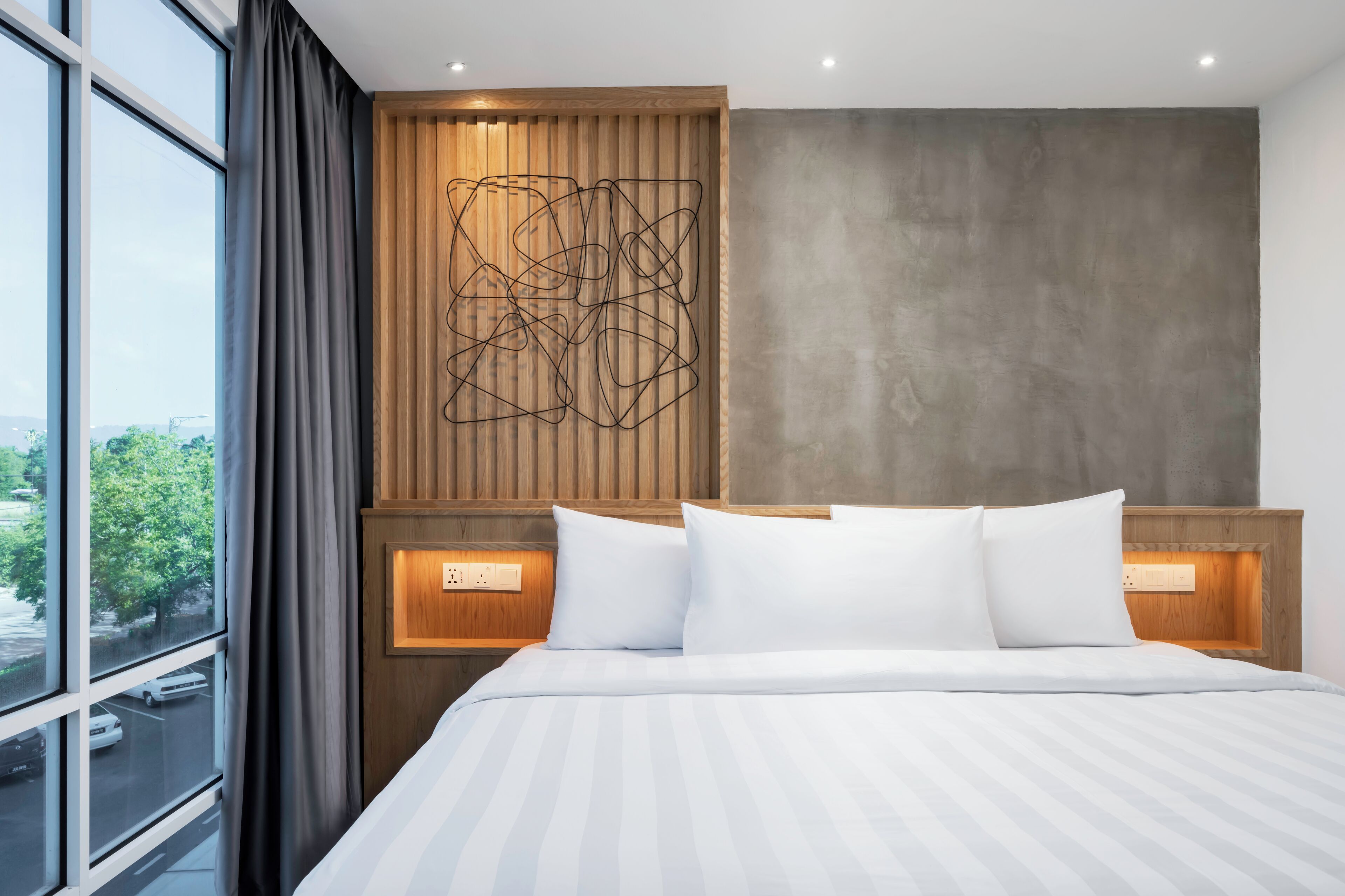 Ett modernt hotellrum med en stor säng, ett träbeklätt sänggavel och utsikt över staden genom fönstret.