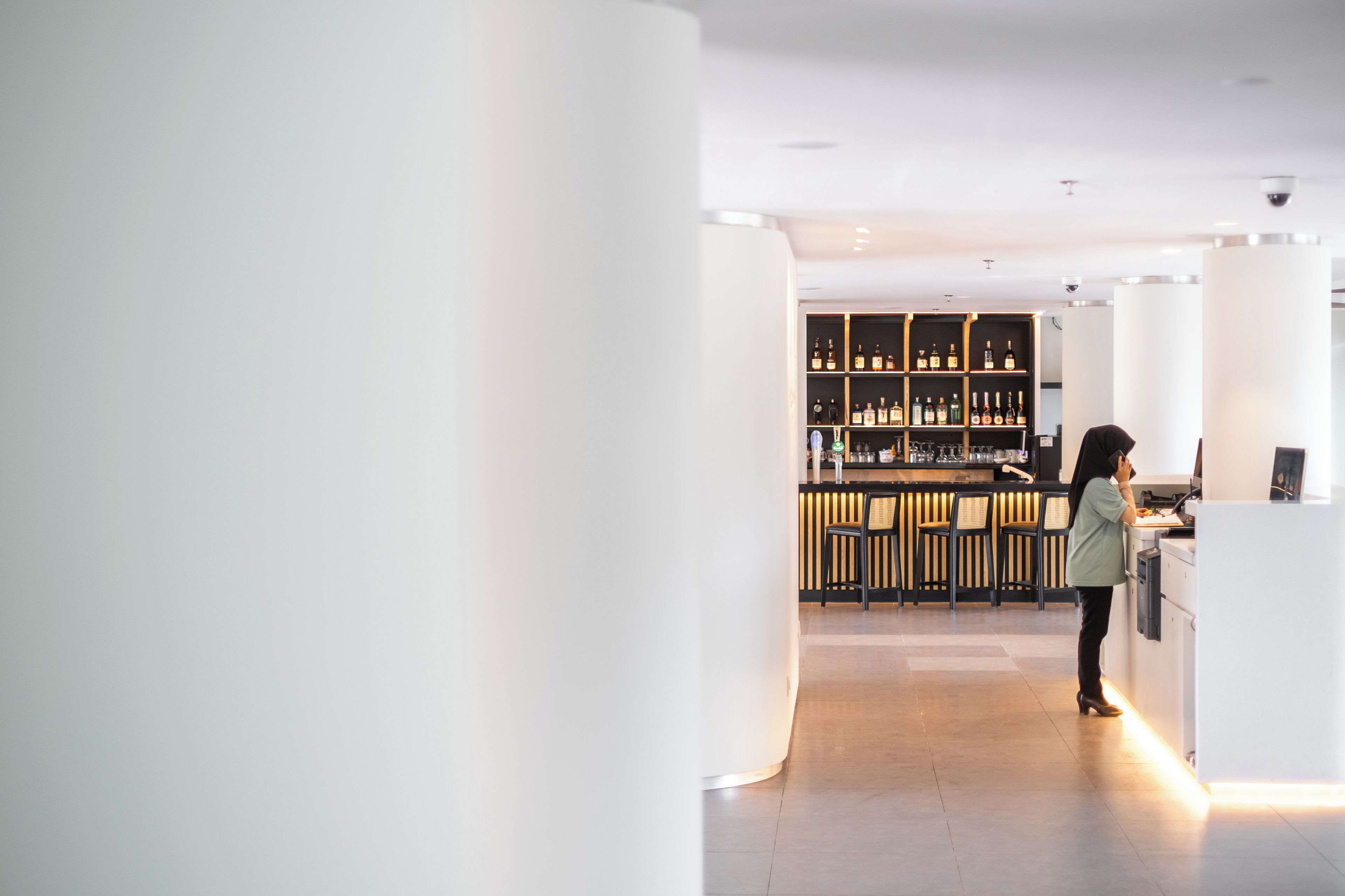 Un intérieur moderne avec un espace bar, des piliers blancs et une personne debout près du bar.
