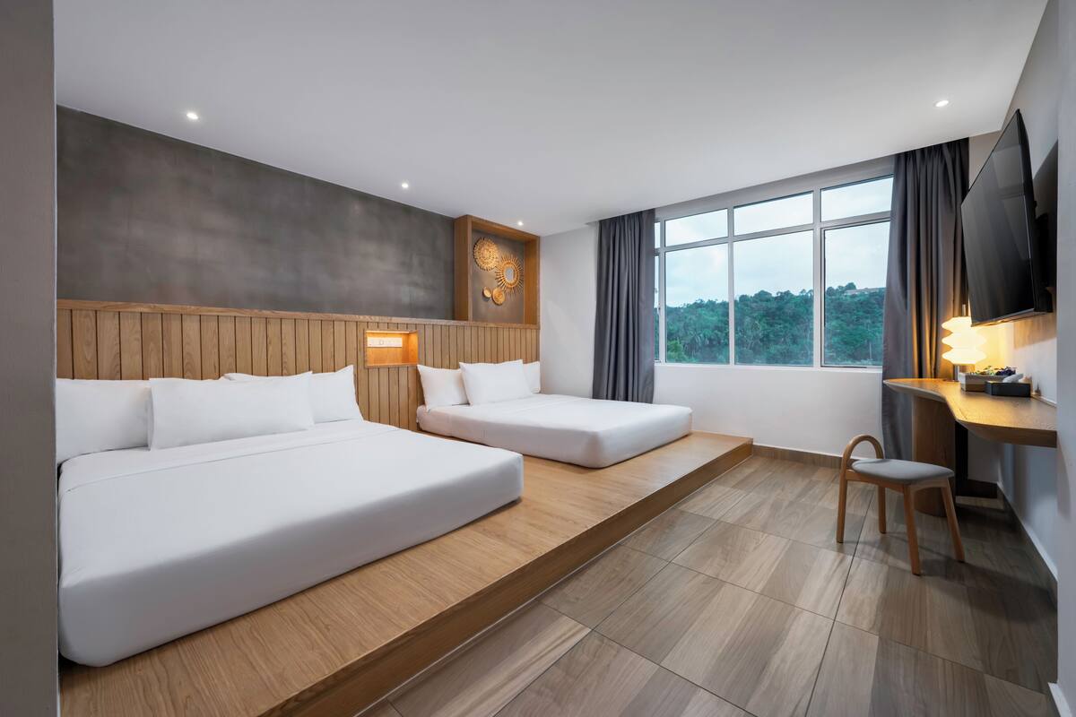 Une chambre d’hôtel moderne équipée d’un grand lit, d’un lit plus petit, d’un bureau, d’une chaise, d’une télévision et d’une fenêtre donnant sur l’extérieur.