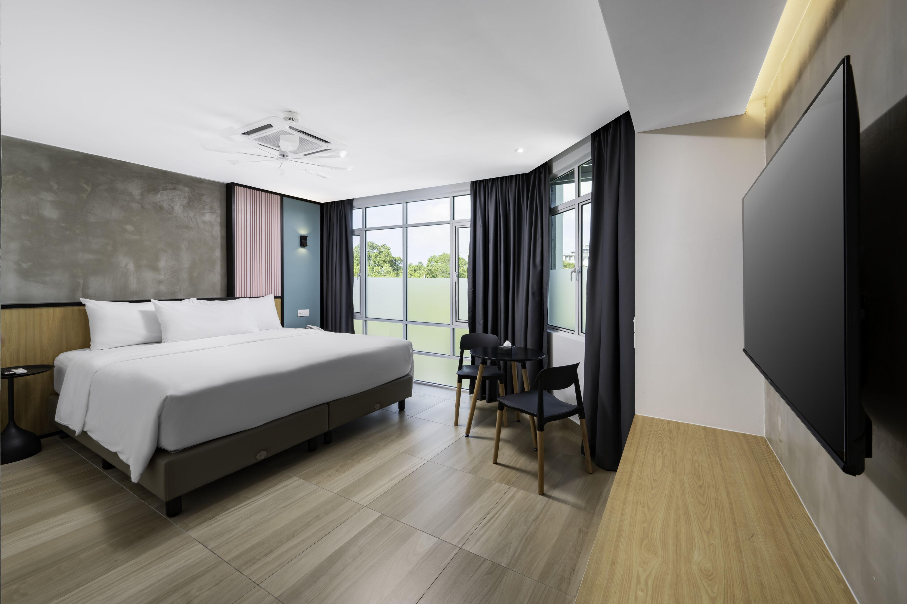 Ein modernes Hotelzimmer mit einem großen Bett, einem Schreibtisch mit Stühlen, einem Flachbildfernseher und einem großen Fenster mit Blick auf die Stadt.