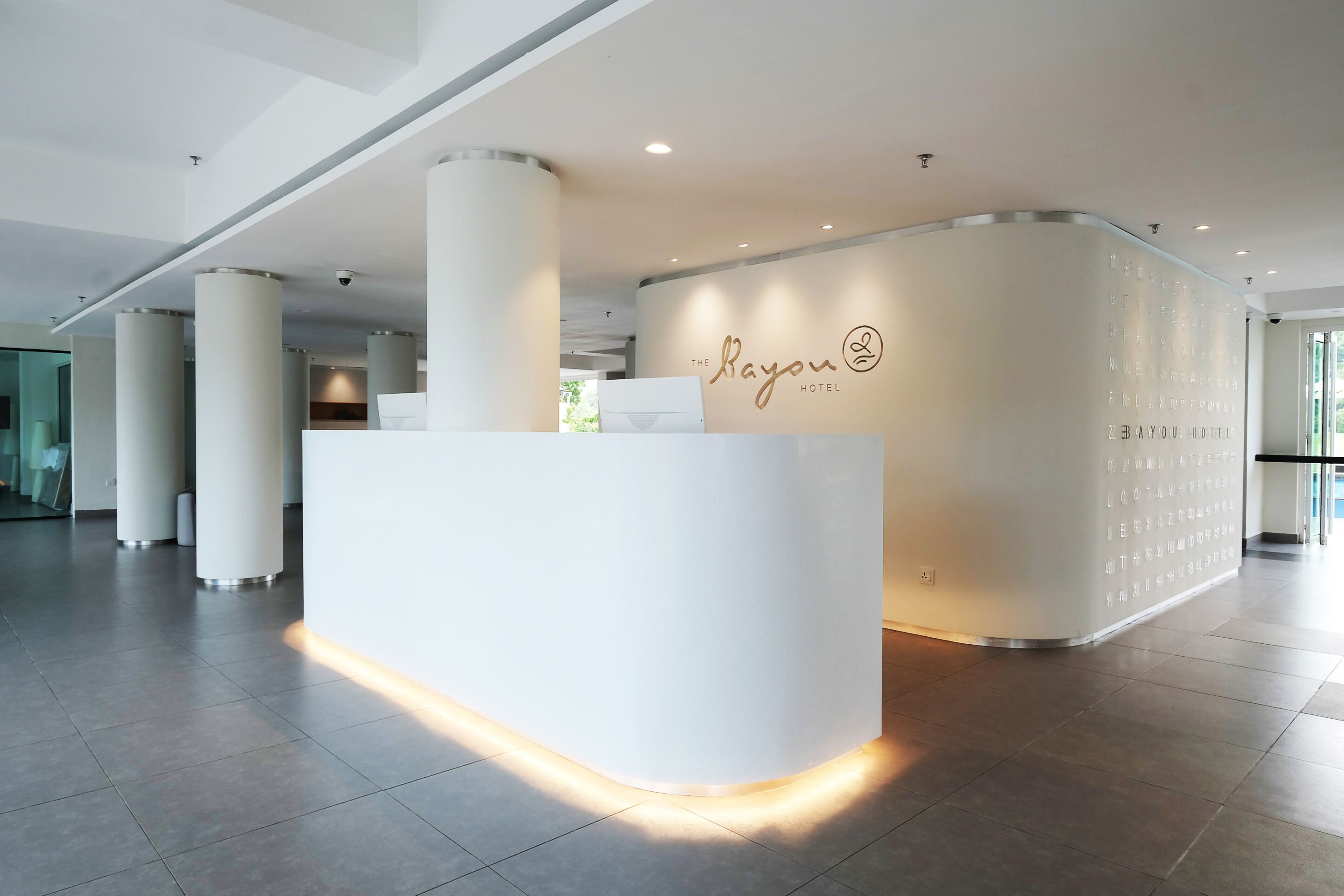 Ein moderner Hotel-Empfangsbereich mit einem weißen Empfangstresen und einer gewölbten Wand, die den Namen des Hotels zeigt.