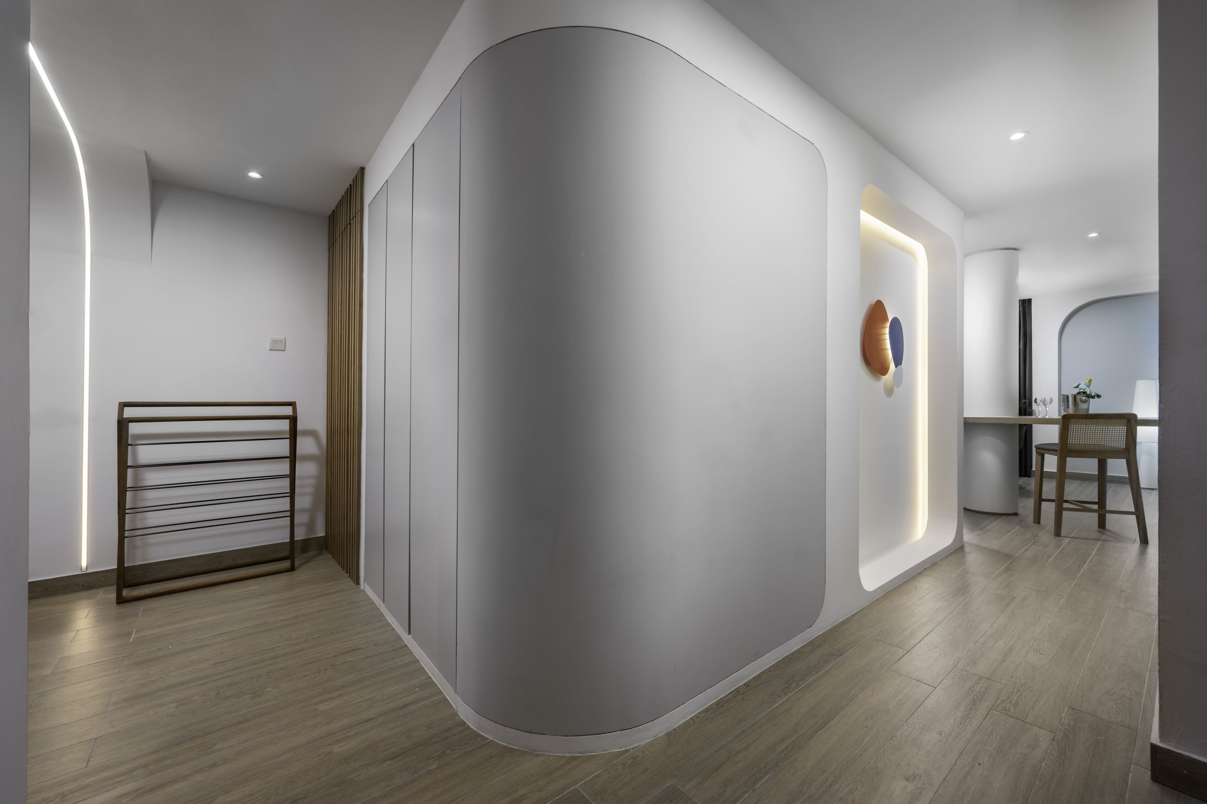 Ein modernes Zimmer mit bogenförmiger Wand, Holzboden, Schreibtisch mit Stuhl und einer Wandablage.