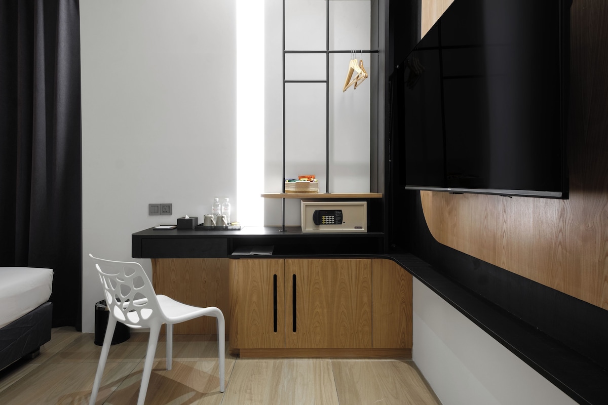 Une chambre d’hôtel compacte comprenant un coin cuisine, un lit simple, une chaise blanche et un téléviseur.