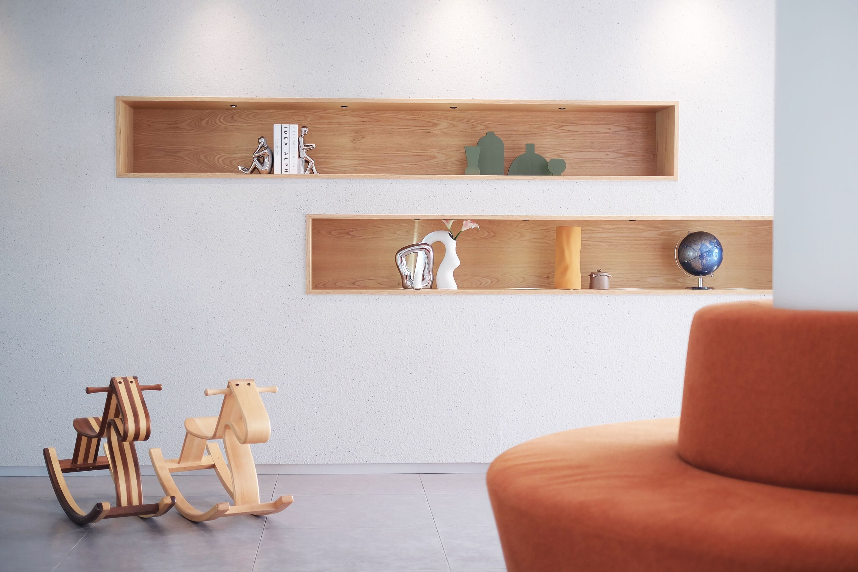 A modern interior with wooden shelves displaying decorative items, a rocking horse, and a plush orange chair.