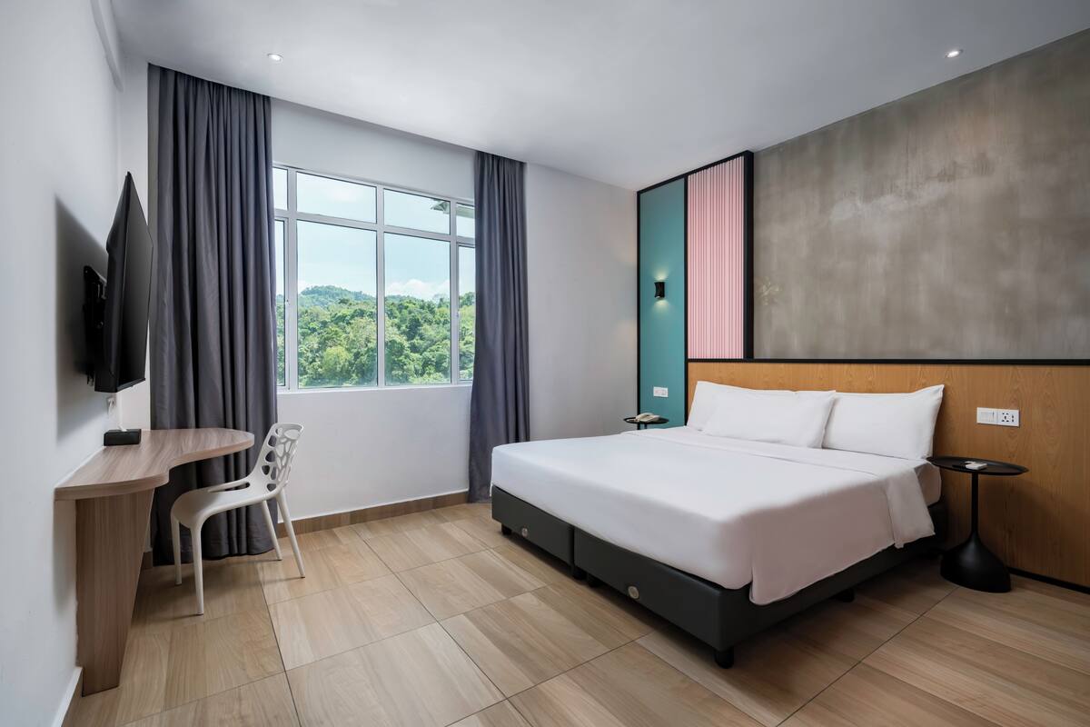 Une chambre d’hôtel moderne dotée d’un grand lit, d’un bureau avec une chaise, d’une télévision et offrant une vue sur la verdure par la fenêtre.