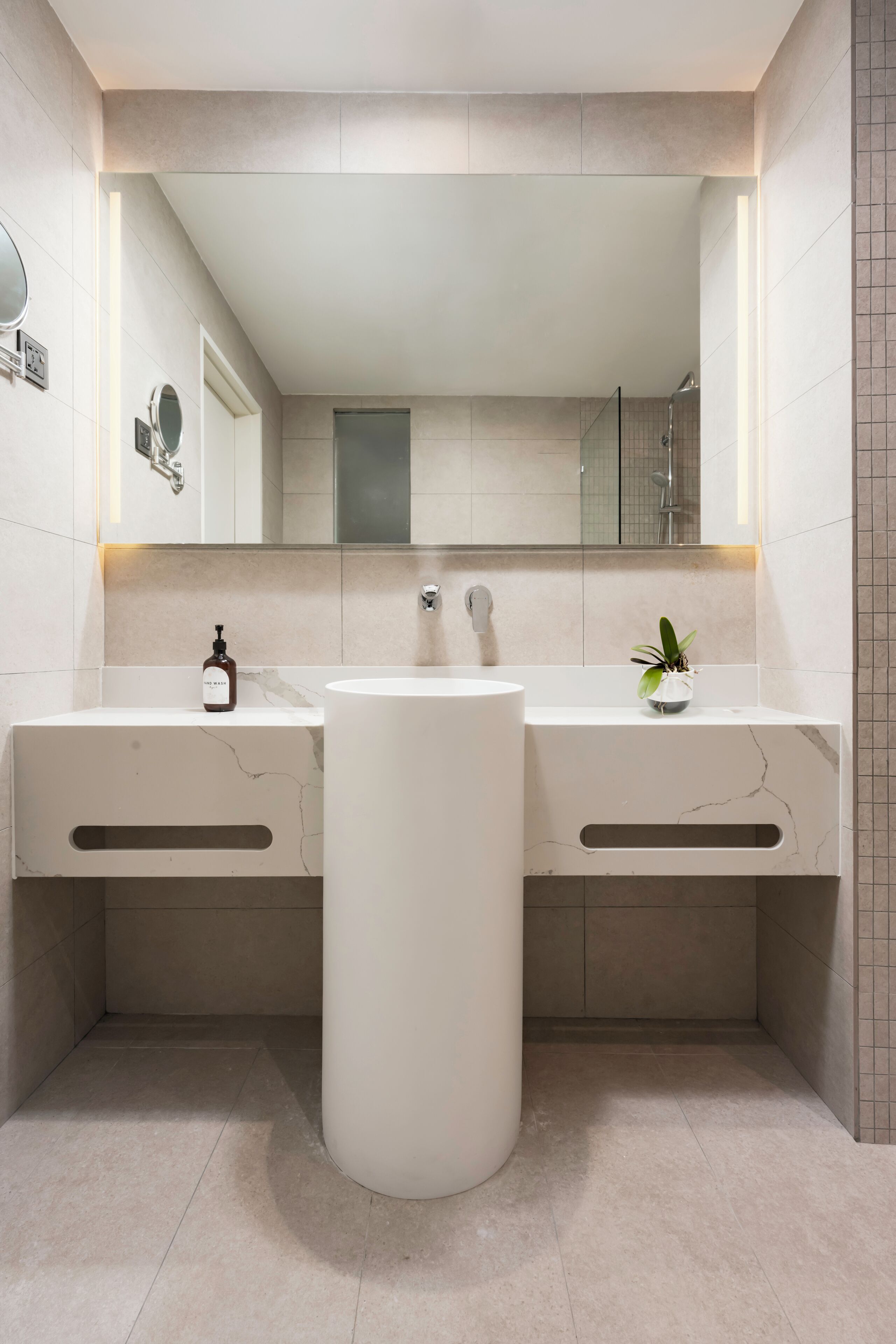 A modern bathroom with a central sink, two vanity mirrors, and a potted plant.