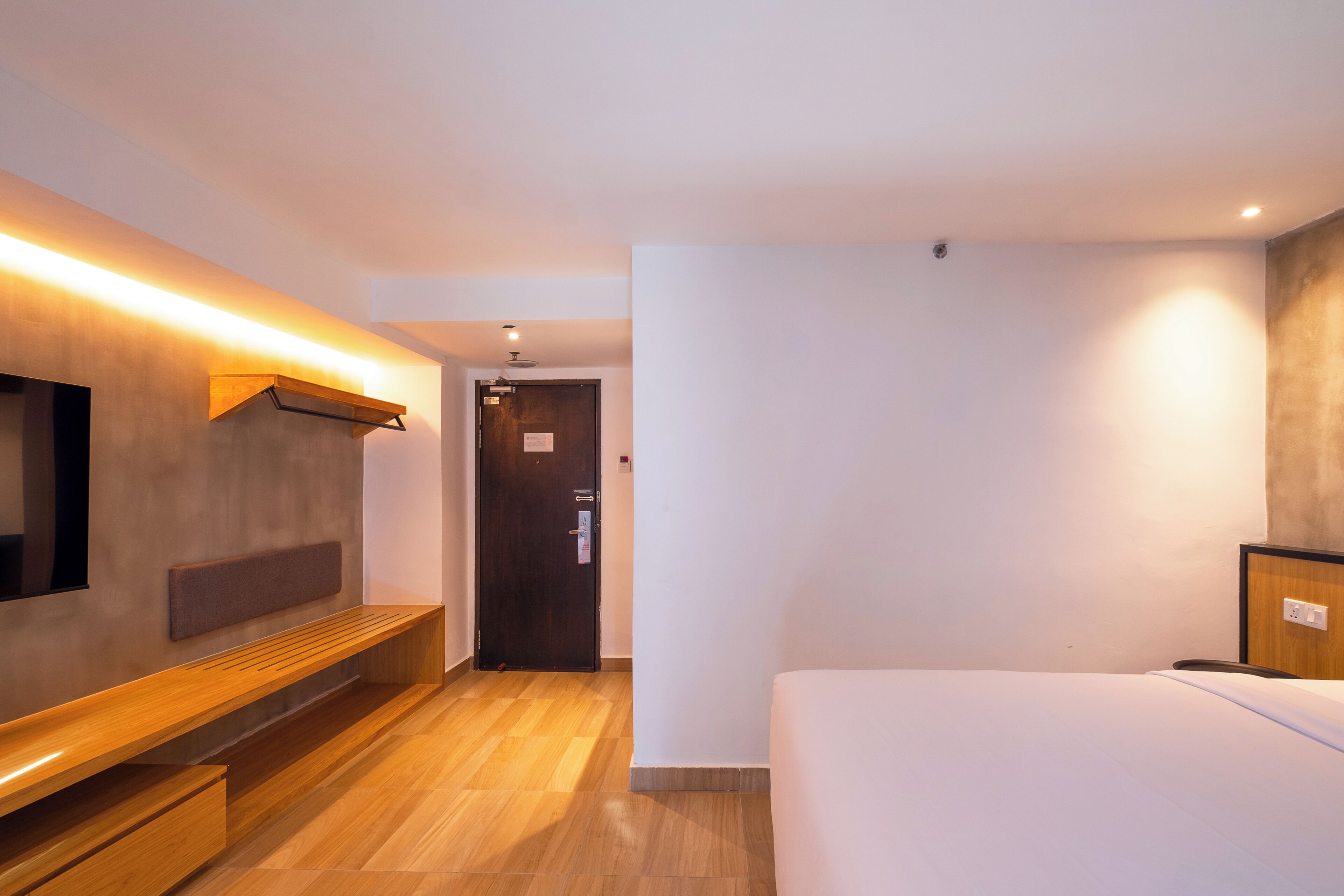 Ein Hotelzimmer mit einem Bett, einer Sitzbank, einem Fernseher und einer Tür.