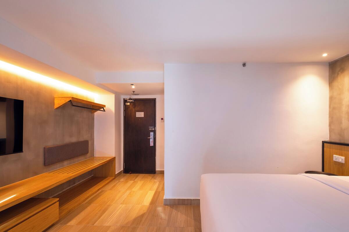 Ein Hotelzimmer mit einem Bett, einer Sitzbank, einem Fernseher und einer Tür.