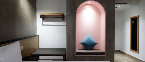 A modern hotel room with a bed, bedside table, and a unique pink archway with a blue pillow.