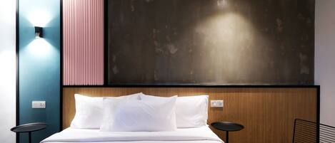 Una habitación de hotel moderna con una cama grande, un cabecero de madera, una mesita redonda y una silla de metal negro.