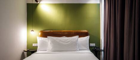 Een hotelkamer met een bed, nachtkastje, lamp en een groene wand.