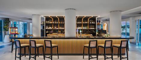 A modern bar area with a central counter, four bar stools, and shelves stocked with bottles.