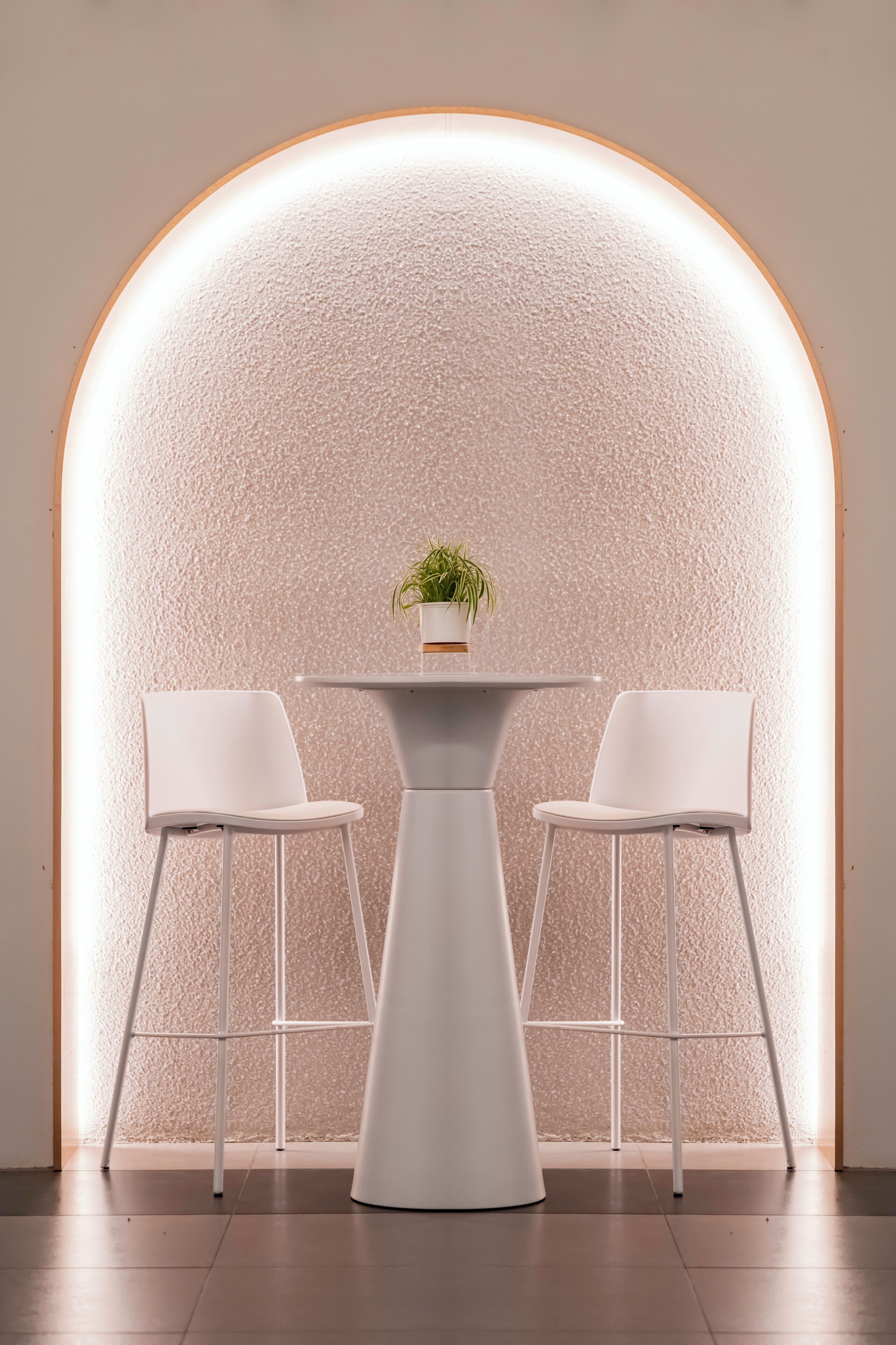 Une pièce moderne avec une table blanche et deux chaises blanches, une plante en pot sur la table et un mur à motifs en arrière-plan.