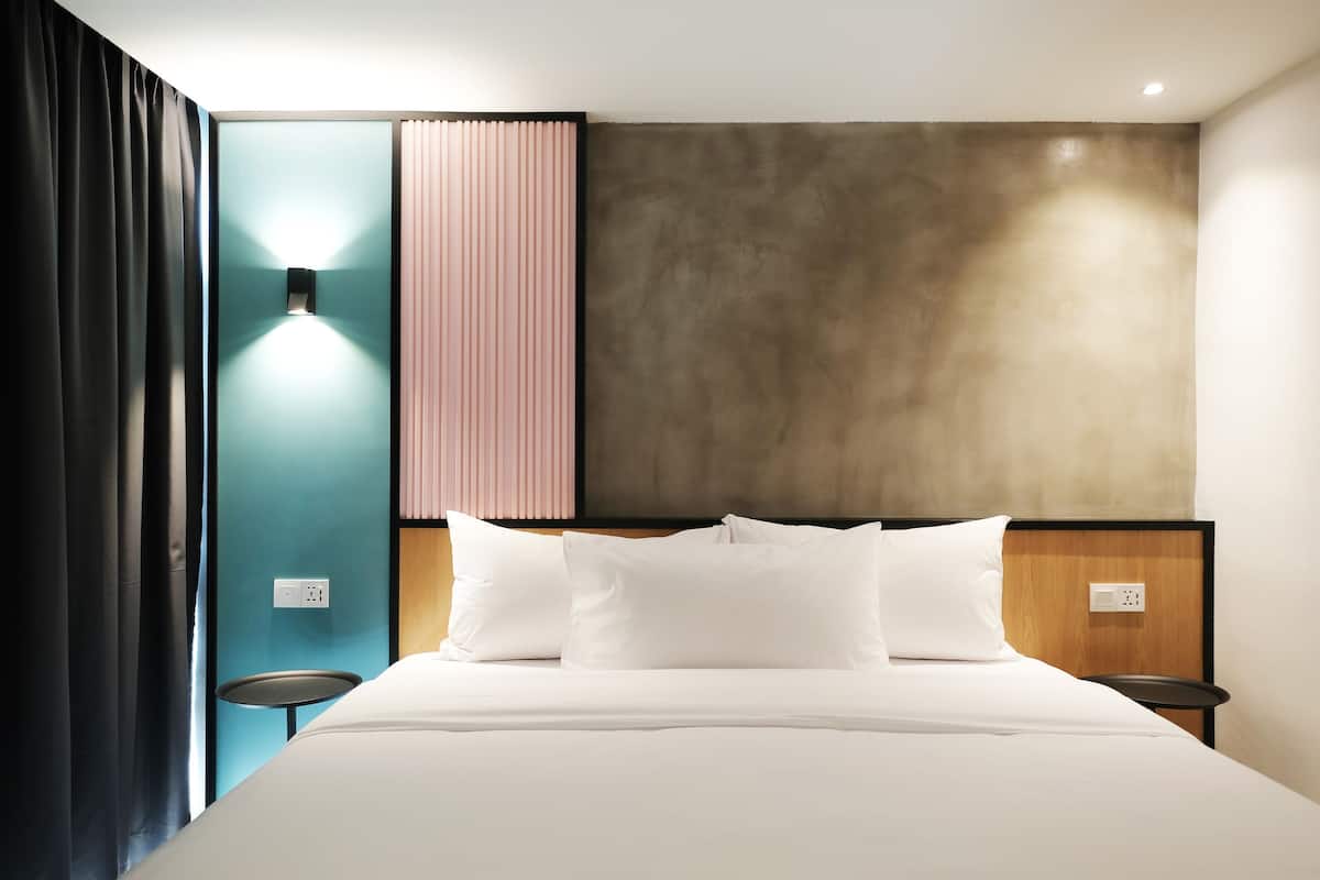 Une chambre d’hôtel moderne équipée d’un lit, de tables de chevet, d’une lampe fixée au mur et d’une prise de courant.