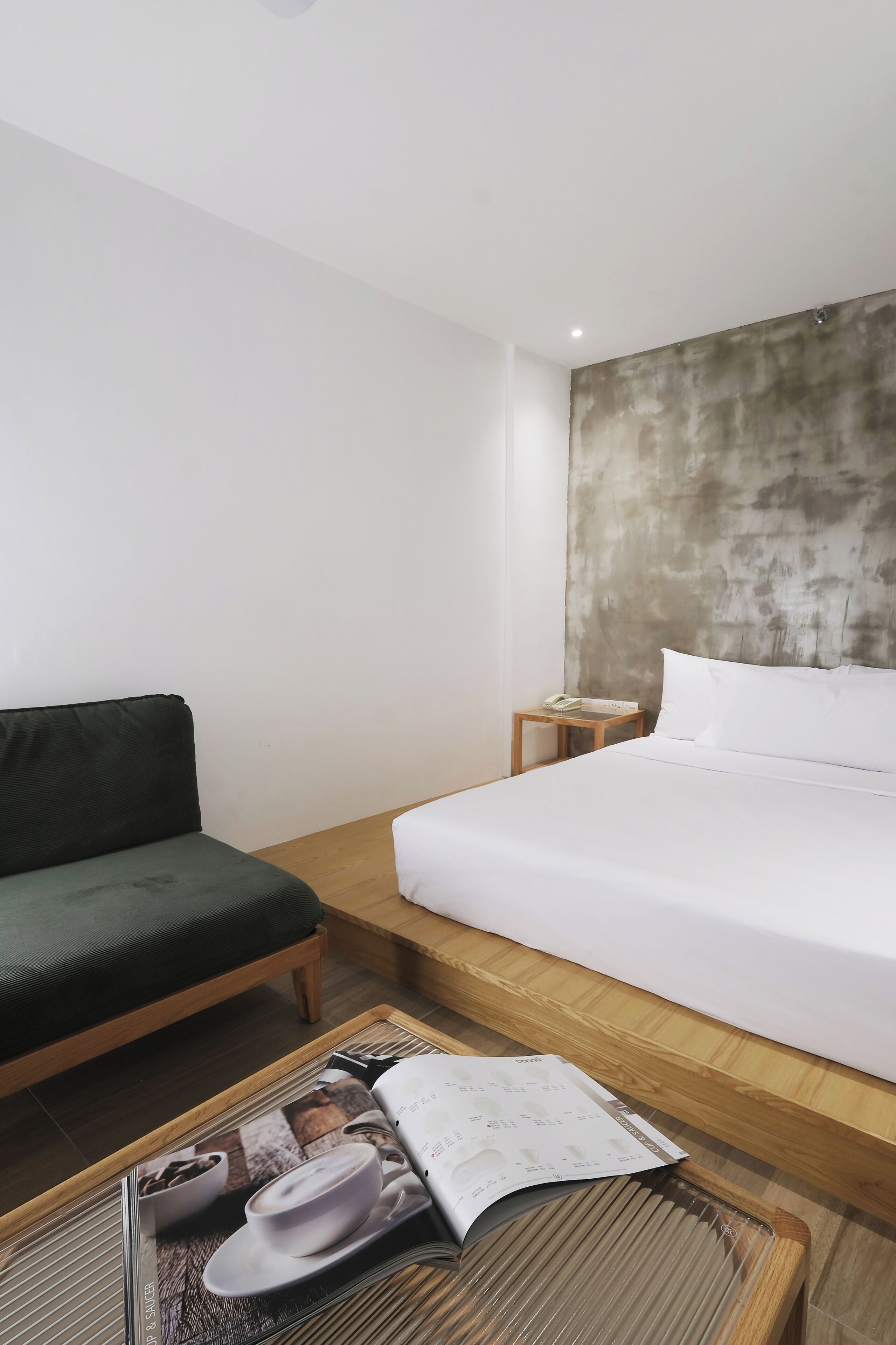 A hotel room with a bed, a green sofa, a wooden nightstand, and a magazine on a coffee table.
