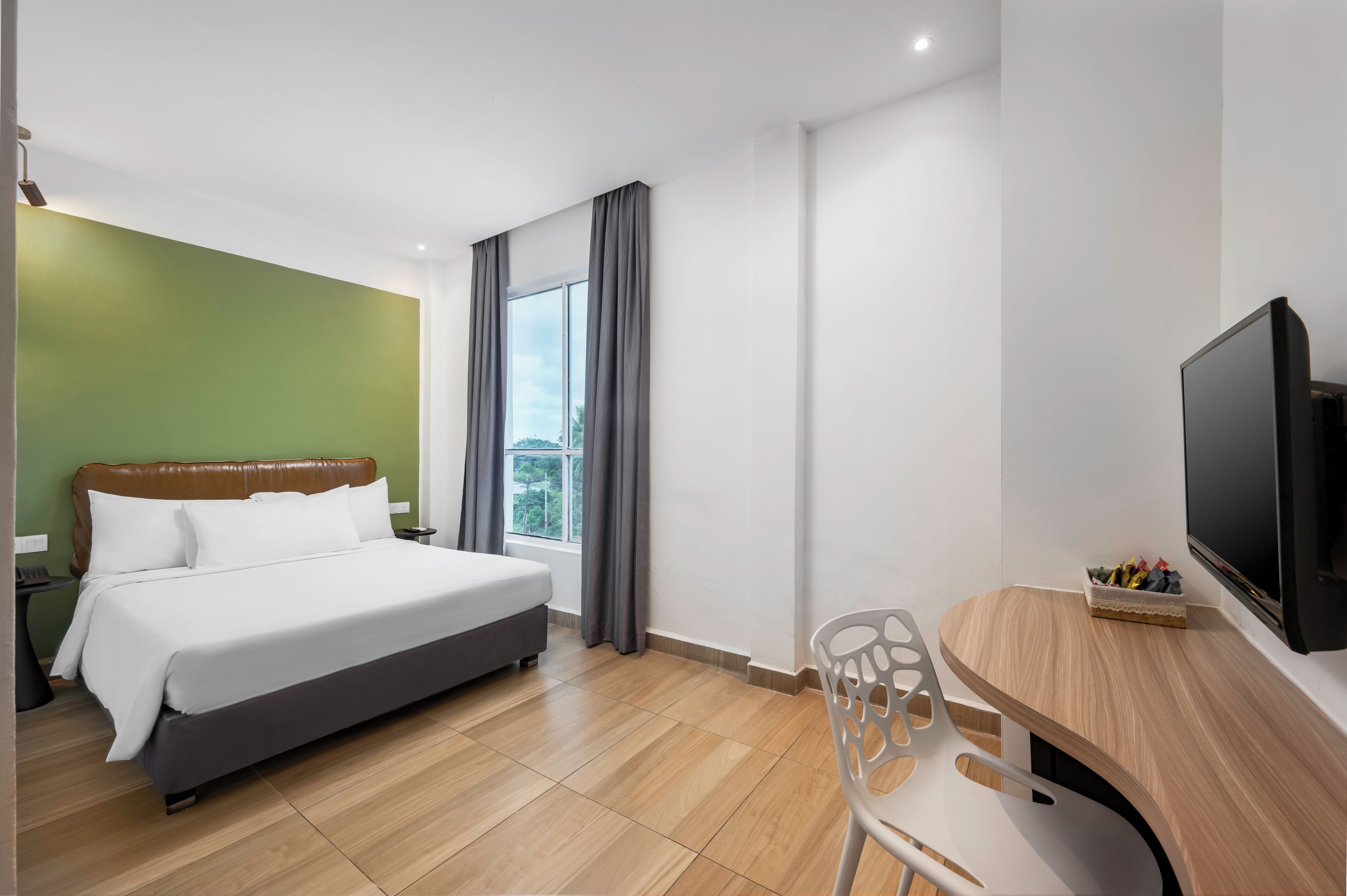 A hotel room with a bed, a desk with a chair, a television, and a window with curtains.